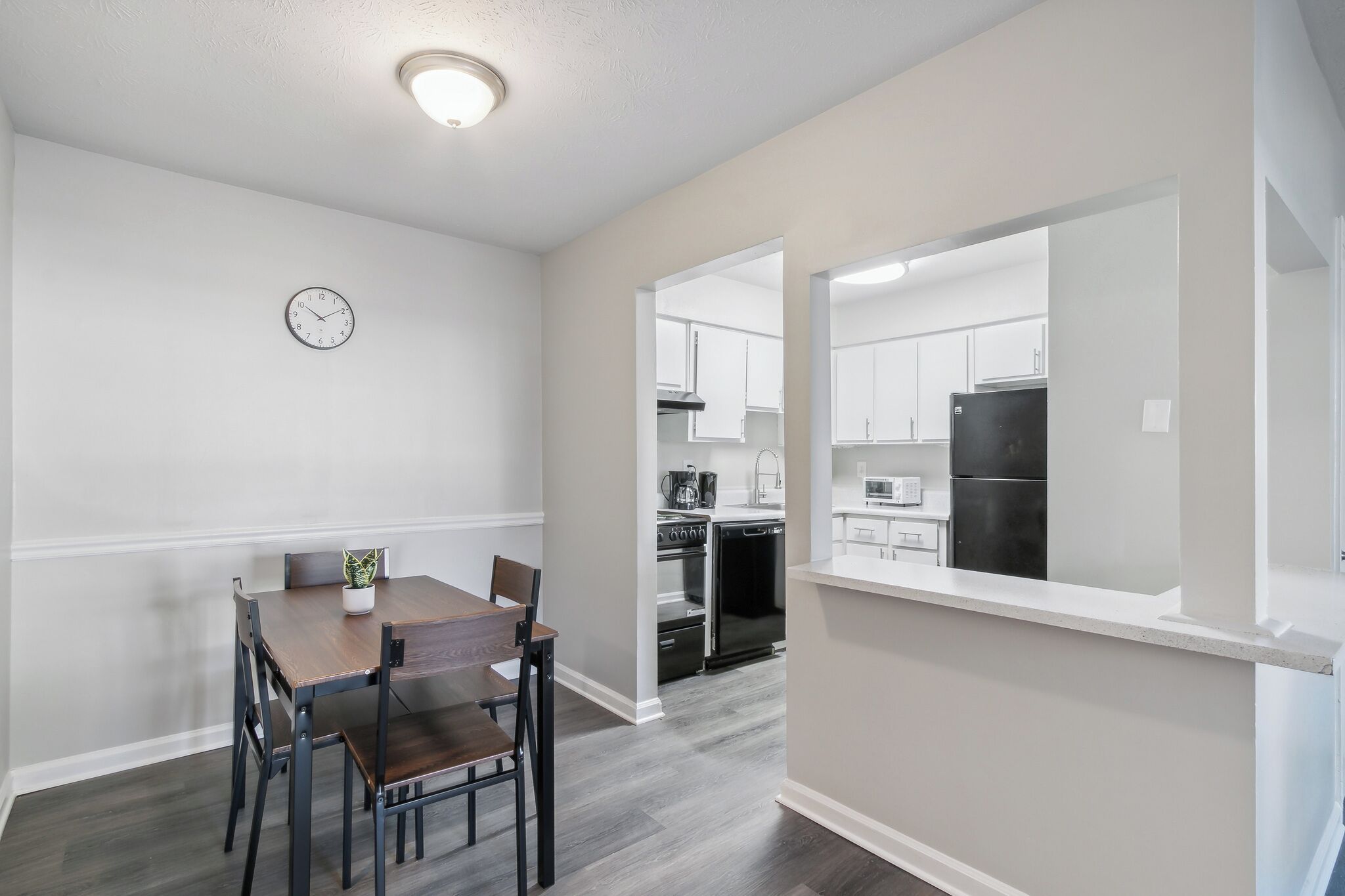 Una cocina moderna con armarios blancos, un refrigerador negro y un comedor con mesa y sillas de madera.