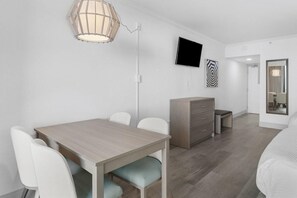 Ein modernes Hotelzimmer mit einem Holztisch, weißen Stühlen, einem Flachbildfernseher, einem Kleiderschrank und einem Spiegel.