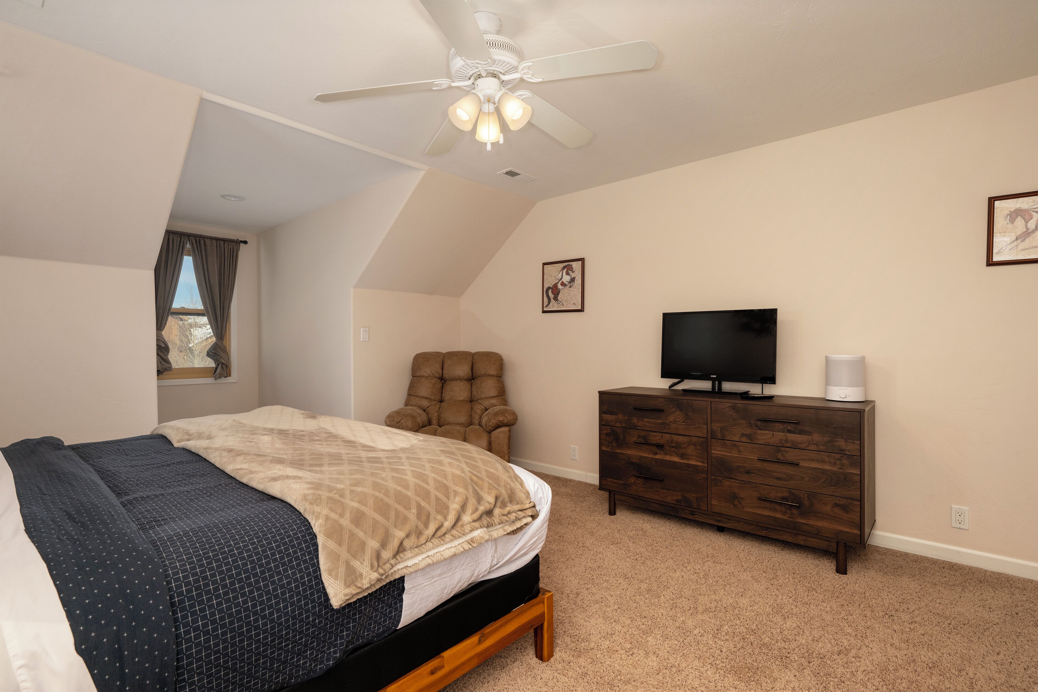 A bedroom with a bed, a chair, a dresser, a television, and a ceiling fan.