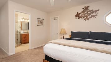 A bedroom with a bed, a ceiling fan, a wall-mounted lamp, and a door leading to a bathroom.