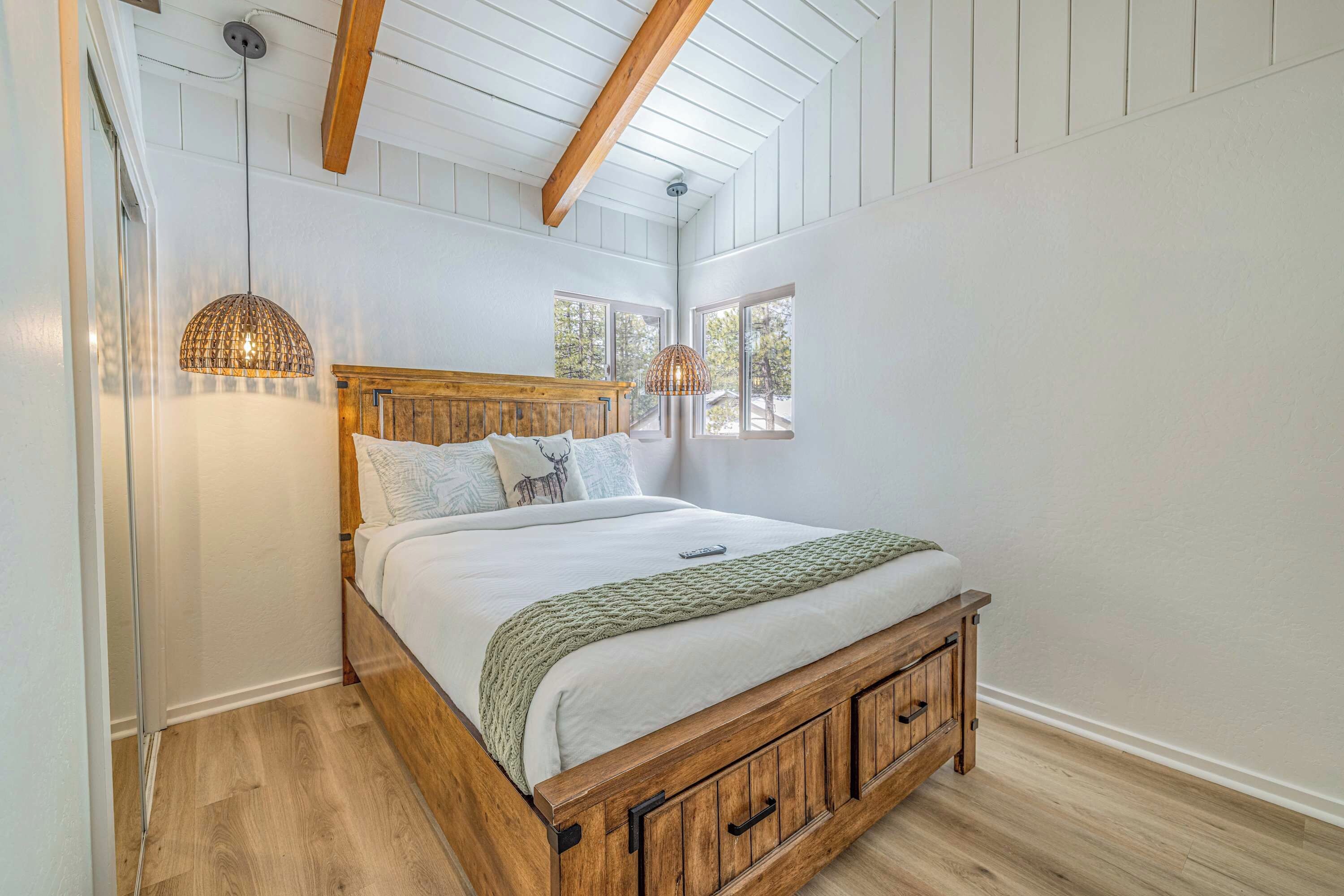 A bedroom with a wooden bed frame, white walls, and a sloped ceiling with exposed beams.