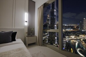 A bedroom with a large window overlooking a cityscape at night.