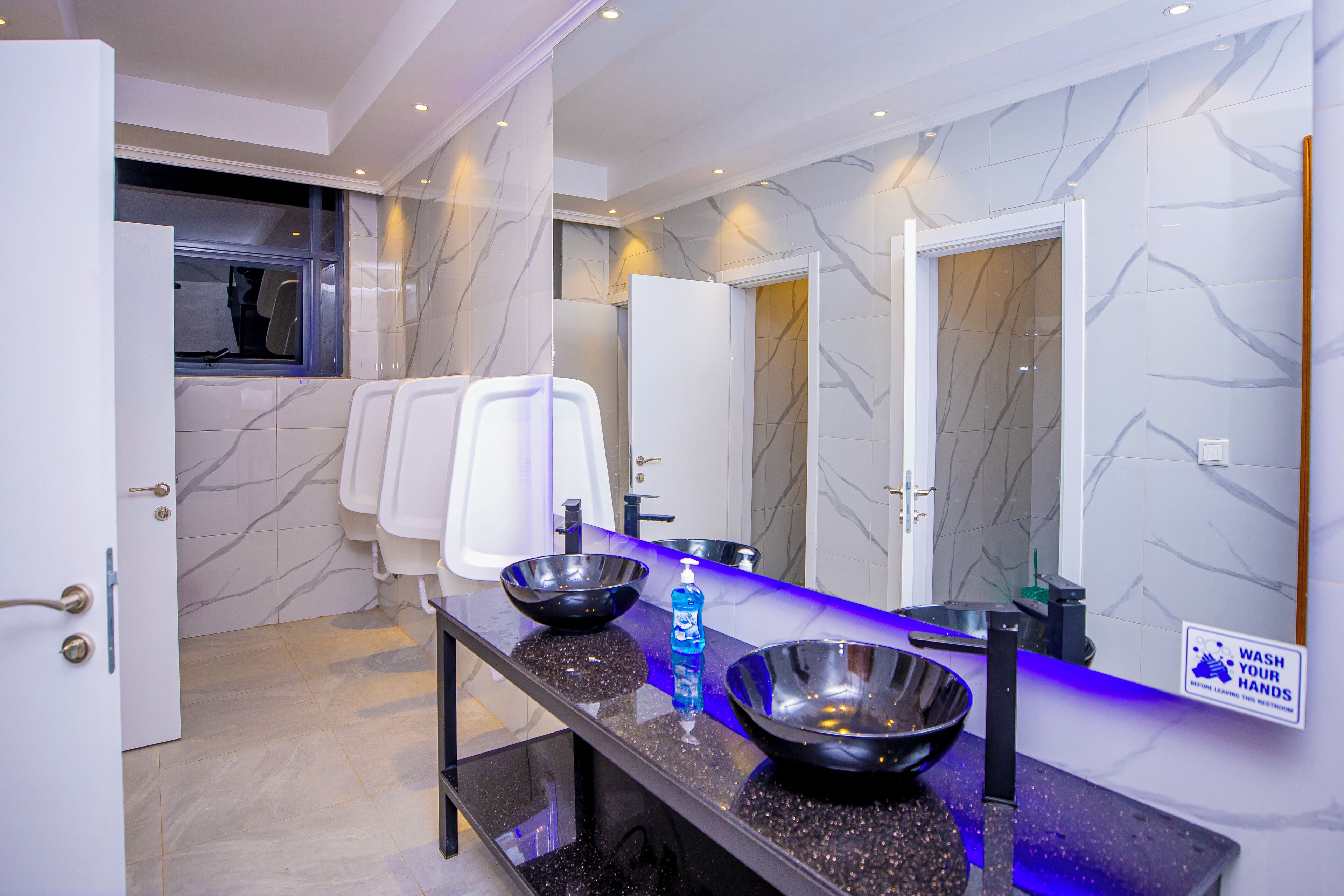 A modern bathroom with a marble wall, a black countertop, and a hand sanitizer dispenser.