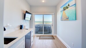 Een moderne keuken met een groot raam, een flatscreen televisie en een schilderij van een strand.