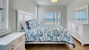 Een slaapkamer met een bed, een dressoir en een plafondventilator. Er is uitzicht op de oceaan door een deur.