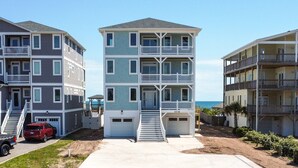 Een meerlaags wooncomplex aan het strand, met een centrale trap, een overdekte veranda en een zichtbare garage.