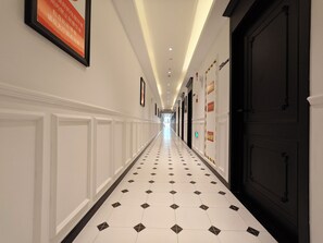 A hotel hallway with a tiled floor, framed pictures on the walls, and a black door on the right. - Jianzhi Erqi Youth Hostel Xihu Branch (Hangzhou)