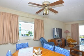 Une pièce avec un ventilateur de plafond, une table à manger sur laquelle se trouve une assiette de condiments, un canapé, un téléviseur et une chaise.