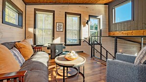 A cozy room with a wooden ceiling, large windows, a ceiling fan, and a round table with a bowl of cookies. - Appalachian Escape: Honeymoon, Hot Tub, Wifi, Games, Fire Pit, Prime Location (Sevierville)
