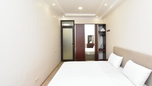 Une chambre d’hôtel avec un grand lit, une armoire, un miroir et une petite étagère contenant des articles de toilette.