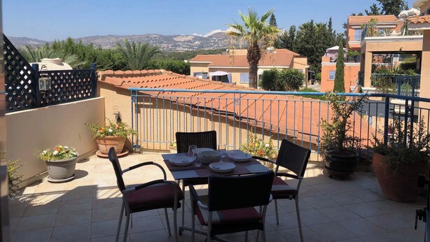 Une terrasse avec une table dressée pour le dîner, entourée de plantes en pot et offrant une vue sur un quartier résidentiel aux toits recouverts de tuiles rouges.