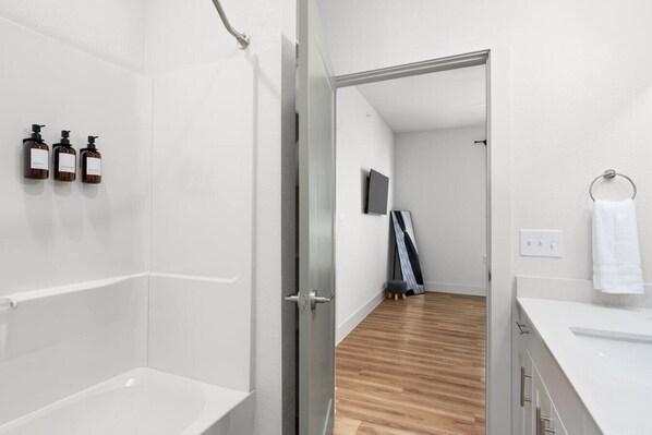 A modern bathroom with a bathtub, a shower, and three bottles of soap on the wall. - Luxury Stay! 1B/1B w/ Gym, Pool, & Shops Nearby (Pflugerville)