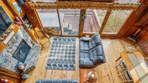 A cozy cabin interior with a stone fireplace, a large sofa, a dining table with chairs, and a view of the surrounding forest. - Valley View Retreat is a tastefully decorated home. Beautiful views The Killington golf course and Green Mountain National Golf Course are just a few minutes from this location. (Killington)