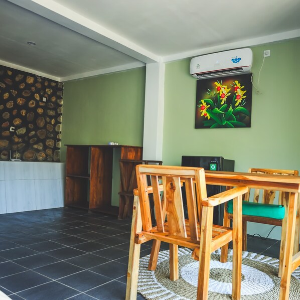 A room with a tiled floor, a wooden dining table with chairs, a wall-mounted air conditioner, and a painting of flowers. - ocean view villas (Kuta)