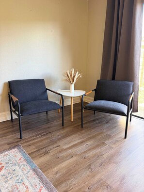 Une pièce comprenant deux chaises de couleur sombre, une petite table blanche et un vase contenant des plantes séchées.