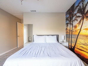 Un dormitorio con cama, mesita de noche, lámpara de pared y puerta que da a otra habitación.