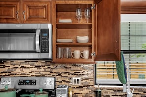 Una cocina con microondas, tostadora y estufa, armarios de madera y salpicadero de azulejos.