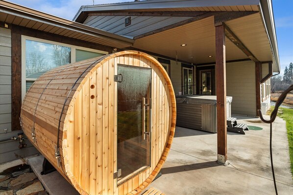 A sauna with a wooden exterior, a glass door, and a concrete floor. - River's Edge! Riverfront with Hot Tub, Sauna & Game Room (Kalispell)