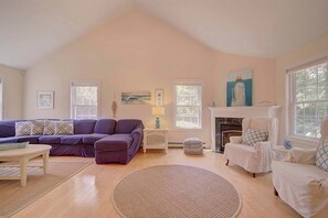 A living room with a high ceiling, a fireplace, a large window, and a cozy seating area.