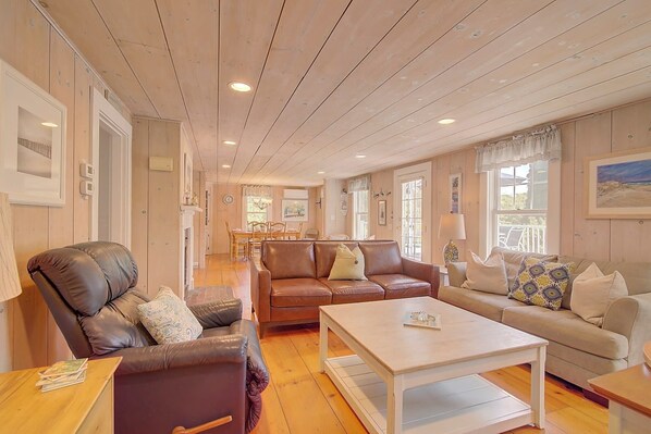A spacious living room with a wooden ceiling, a brown leather sofa, a beige sofa, and a white coffee table. - Large Deck, Fire Pit, Dog Friendly, Near Beach - Sleeps 10! (Harwich)