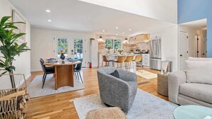 A spacious living room with a dining area, kitchen, and a large window. - Game Room,  Private Yard w Fire Pit! (Harwich)