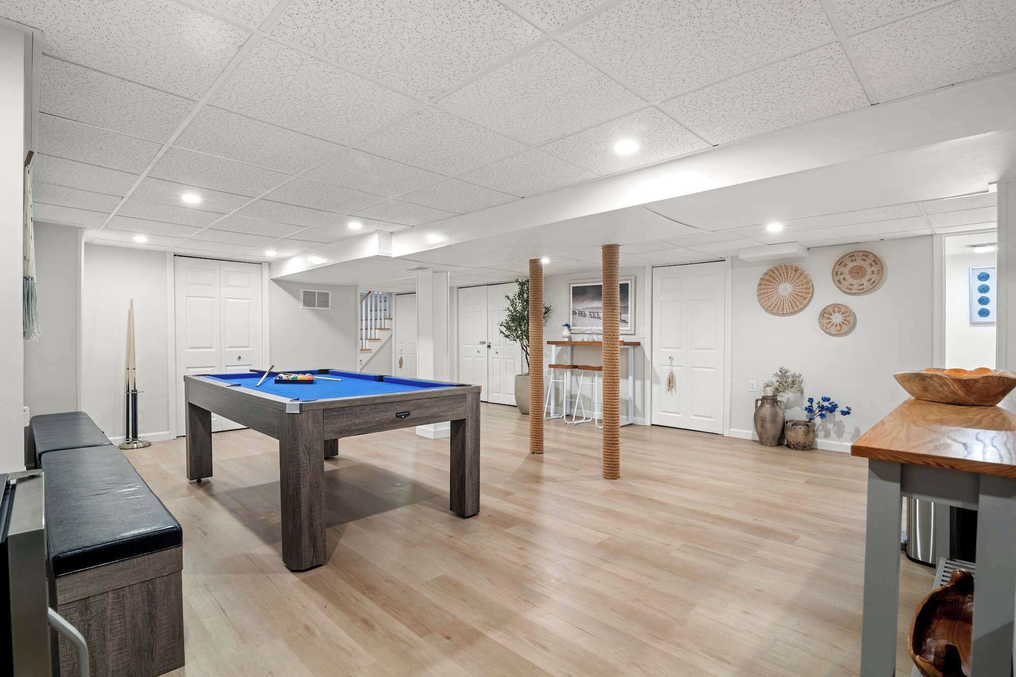 A modern indoor space with a pool table, a staircase, and a wooden bench.