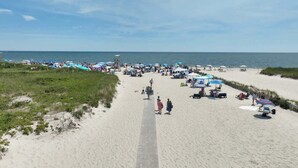 A beach with a wooden boardwalk leading to the water, surrounded by umbrellas and beachgoers. - Game Room,  Private Yard w Fire Pit! (Harwich)