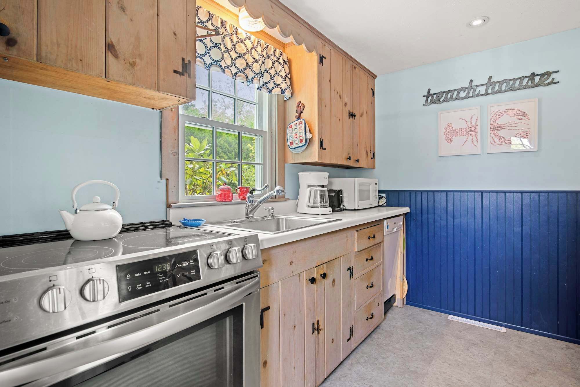 Une cuisine avec des meubles de rangement en bois, une cuisinière, un évier et une fenêtre donnant sur un paysage verdoyant.