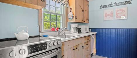 Une cuisine avec des meubles de rangement en bois, une cuisinière, un évier et une fenêtre donnant sur un paysage verdoyant.