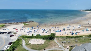 Une plage avec de nombreux parasols et beaucoup de monde, un parking et une vue dégagée sur l’océan.