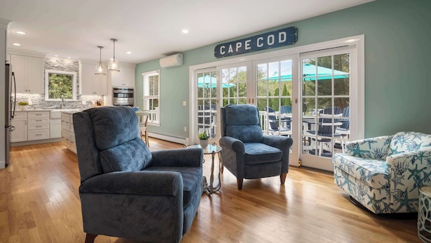 Un intérieur moderne comprenant une cuisine, deux fauteuils bleus, un canapé à motifs et un panneau indiquant « Cape Cod ».