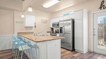 Una cocina moderna con armarios blancos, electrodomésticos de acero inoxidable y una isla central con taburetes de bar.