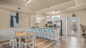 Una cocina moderna con armarios blancos, una isla central con taburetes de bar y un comedor con mesa de madera y sillas blancas.