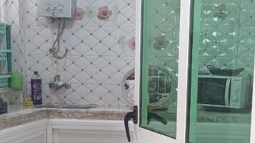 Un baño con ducha, inodoro y lavamanos. Se observa una ventana con marco verde y un calentador de pared blanco.
