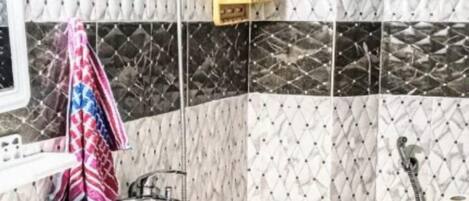 A bathroom with a white sink, a shower, and a toilet. There is a towel hanging on the wall and a shelf with toiletries.