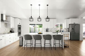 A modern kitchen with white cabinetry, stainless steel appliances, and a central island with bar stools.
