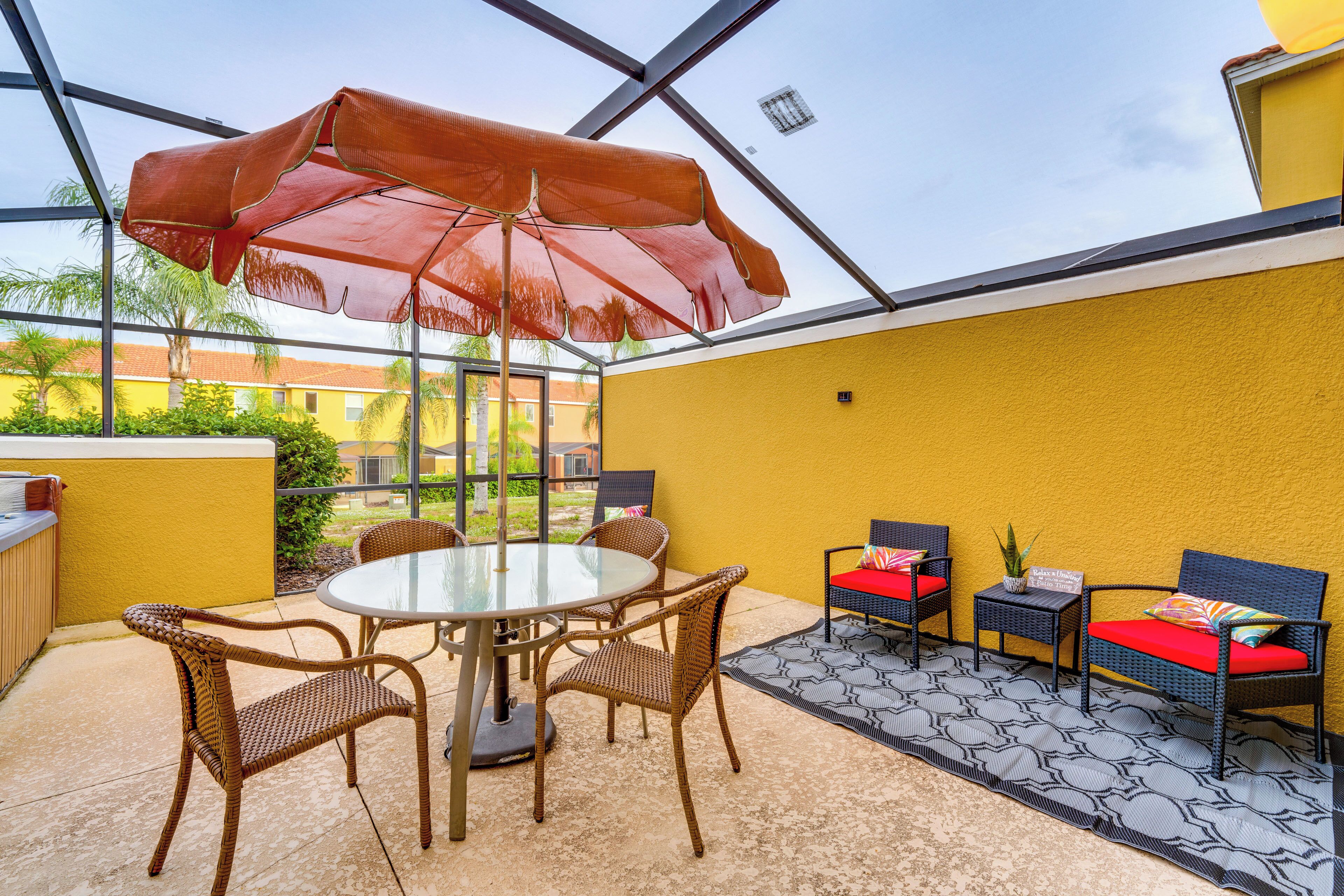 A covered patio area with a table and chairs, a small table with a plant, and a yellow wall.