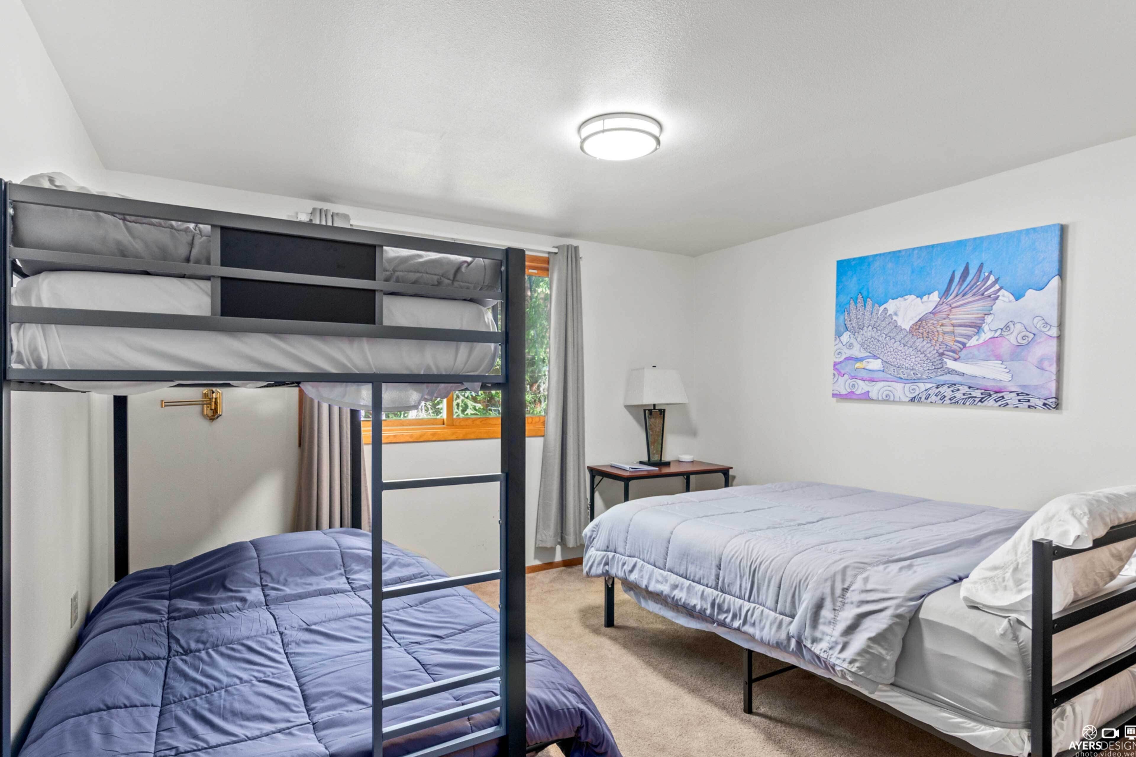 A room with bunk beds, a bedside table with a lamp, and a painting on the wall.