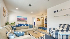 Una sala de estar con sofá, mesa de centro y sillones, un comedor con mesa y sillas, y una cocina al fondo.