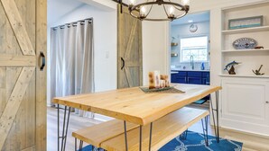 Una mesa de comedor de madera con bancos, una araña y decoración náutica en una cocina y comedor luminosos.