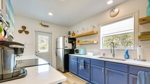 Una cocina moderna con refrigerador, microondas y cafetera. Se aprecia una ventana con vista a árboles y un reloj en la pared.