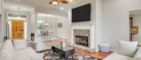 A spacious living room with a fireplace, a ceiling fan, and a flat-screen TV mounted above it.
