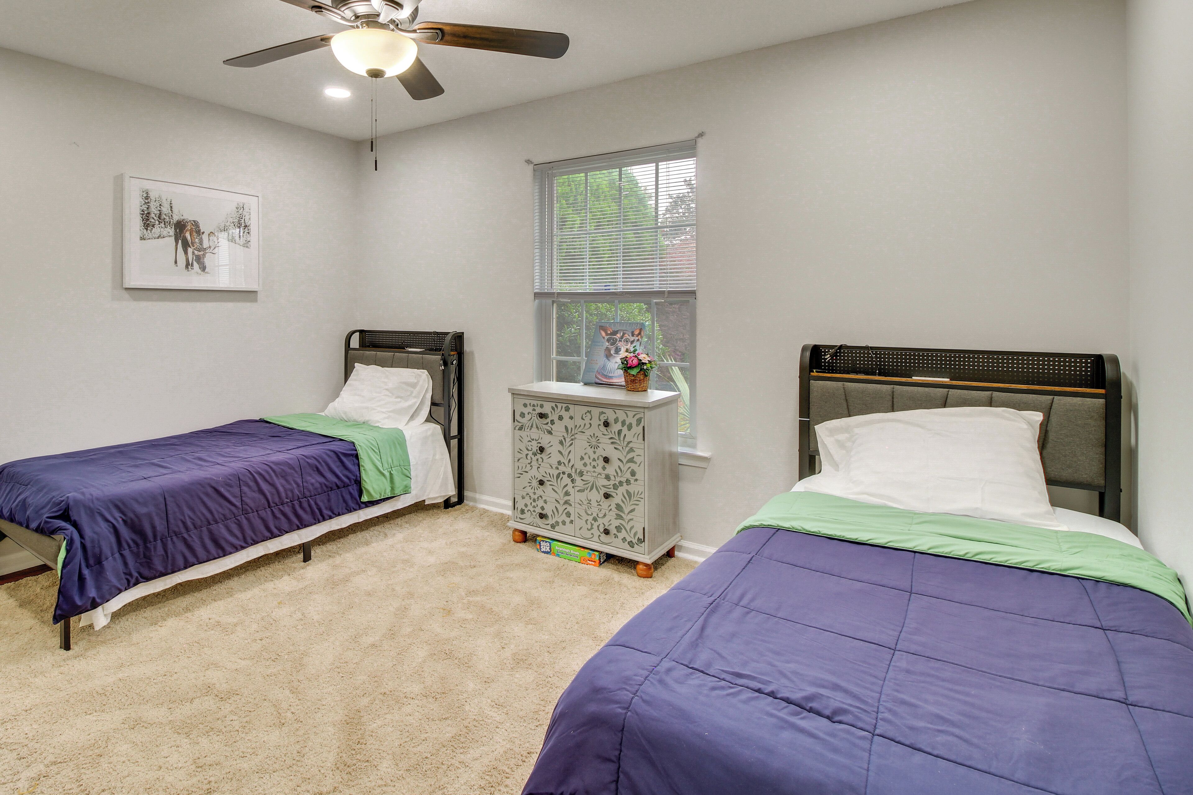 A bedroom with two single beds, a nightstand, a window with blinds, and a ceiling fan.