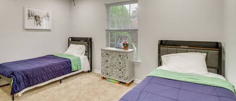 A bedroom with two single beds, a nightstand, a window with blinds, and a ceiling fan.
