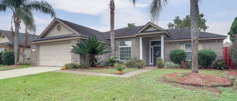 A residential house with a garage, a well-maintained lawn, and palm trees.