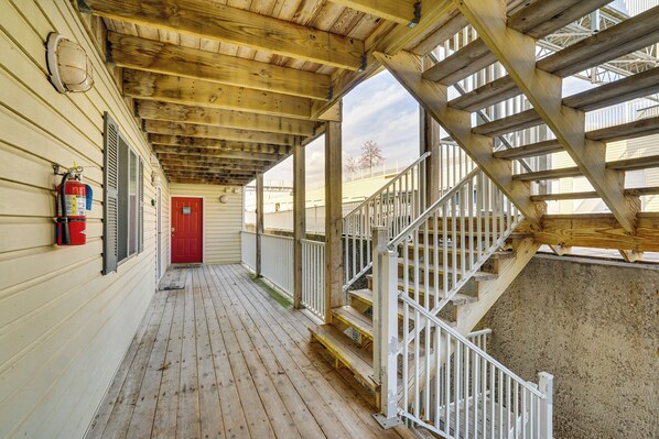 A covered wooden deck with a red door, white railings, and a fire extinguisher mounted on the wall. - Lakefront Osage Beach Condo w/ Water-view Balcony! (Osage Beach)