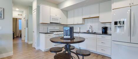 A modern kitchen with white cabinets, a central island with stools, a built-in microwave, and a refrigerator.