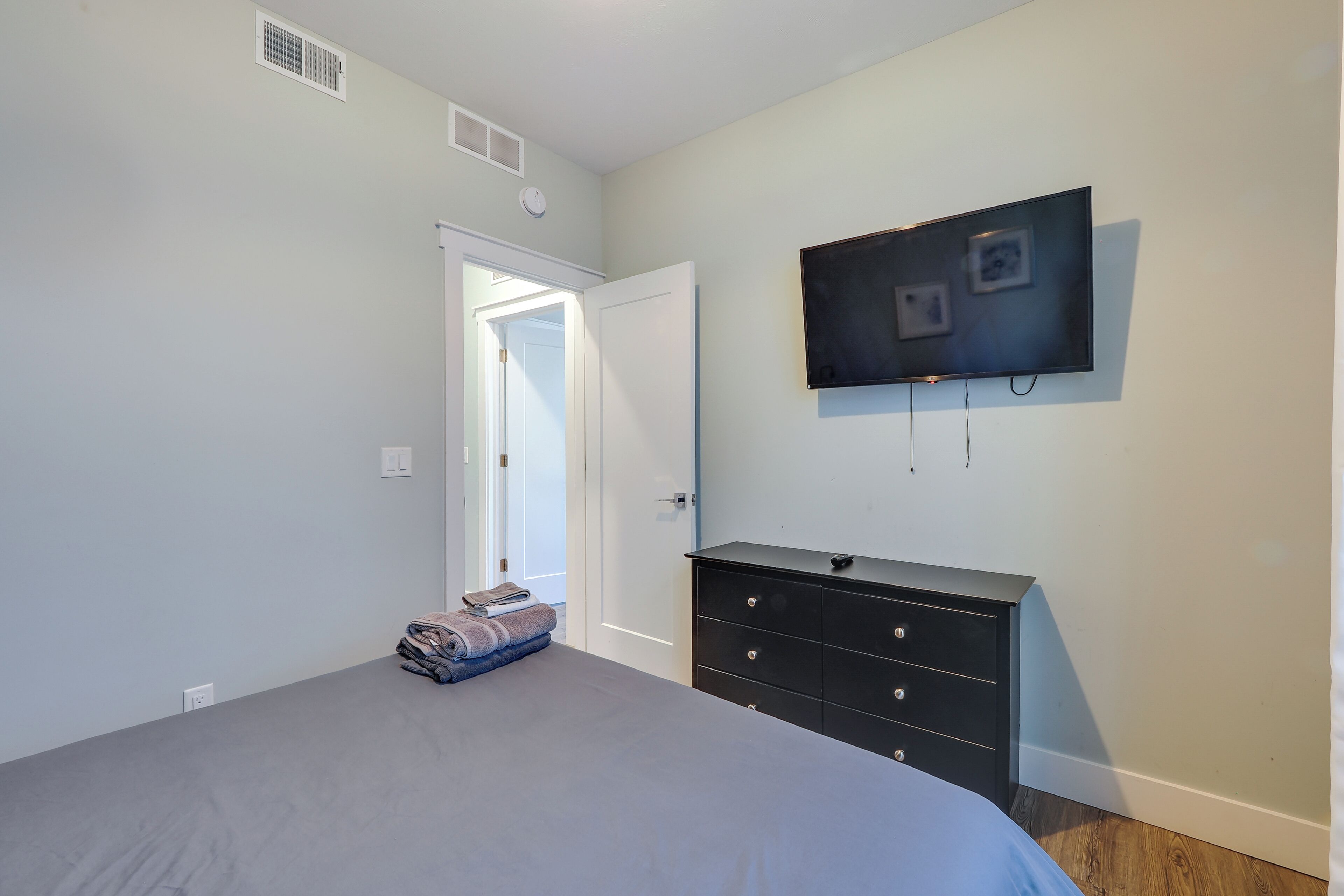 A bedroom with a bed, a dresser, a television mounted on the wall, and a door leading to another room.