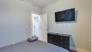 A bedroom with a bed, a dresser, a television mounted on the wall, and a door leading to another room.