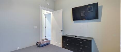 A bedroom with a bed, a dresser, a television mounted on the wall, and a door leading to another room.